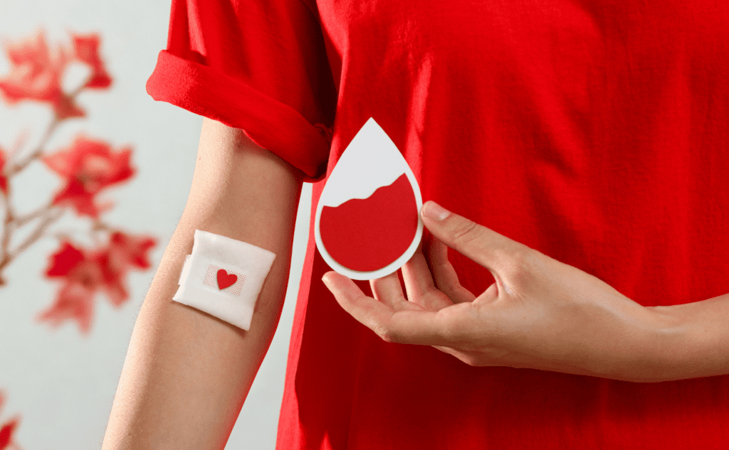 Person holding a blood drop symbol with arm bandage on red background